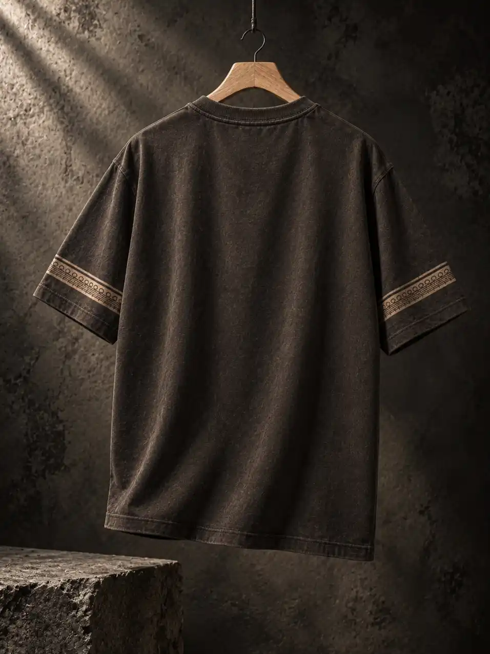 Back view of a men’s graphic T-shirt hanging on a wooden hanger against a dark textured studio wall with dramatic side lighting.