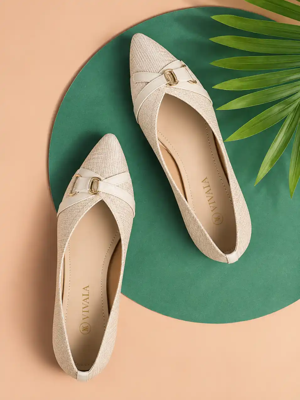 Elegant women’s flat footwear pair photographed from above on a peach and emerald green background with tropical palm leaves.