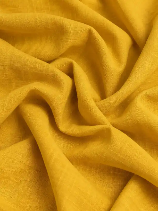 Close-up of mustard yellow linen fabric with natural woven texture and soft flowing folds.